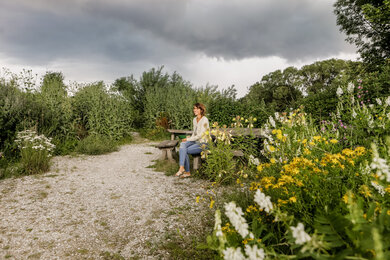 Frau sitzt auf Bank im Permakulturgarten | © @titantina /Tina Vega-Wilson