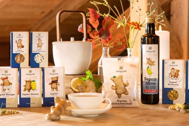 The photo shows the entire Sonnentor ginger product range. The products are on a table together with candles and flowers. | © SONNENTOR