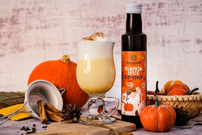 On the picture is a bottle with pumpkin spice syrop and a pumpkin spice latte. In the backgroud is a pumpkin and a lot of spices in a autumn setting. | © SONNENTOR