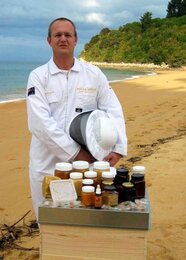 Photo of Bernhard Schneider on the beach. In front of it are many kinds of honey products. | © SONNENTOR