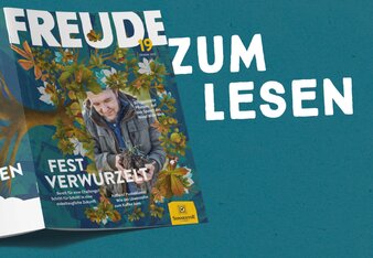 Die Freude Nr. 19 ist aufgeschlagen und liegt mit dem Cover nach oben. Sie zeigt quer liegend über die Vorder- und Rückseite einen Baum mit Wurzeln und Blättern, auf der Vorderseite ist au0erdem ein Mann, der Erde in der Hand hält. | © SONNENTOR