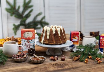 Das Foto zeigt einen weihnachtlich hergerichteten Tisch mit einem Gugelhupf in der Mitte, dem Gewürzadventkalender, Lebkuchenzeit und Zimtzauber Tee daneben und Nüssen in Schälchen und Tannenzweigen drum herum. | © SONNENTOR