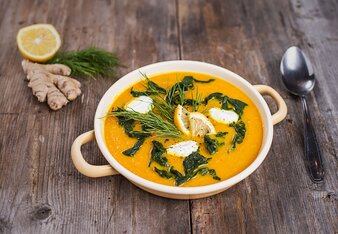 Das Foto zeigt eine orange Cremesuppe mit grünen Blättern, Dillzweigen und Zitronenscheiben als Einlage und Garnitur. | © SONNENTOR