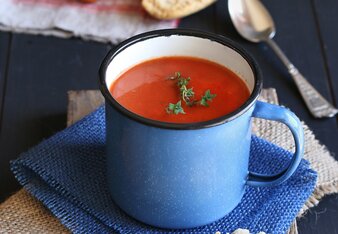 Auf dem Foto sieht man eine Tasse mit Tomatensuppe. Daneben sieht man Baguettes und frische Tomaten. | © SONNENTOR