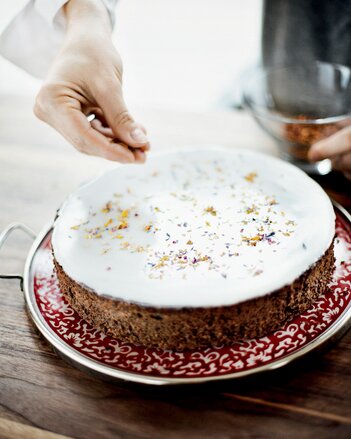 Auf dem Foto ist eine Flower Power Mohntorte zu sehen. Man sieht wie jemand die Gewürzblütenmischung auf die Torte streut. | © SONNENTOR