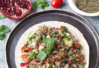 Auf dem Foto sieht man ein Fladenbrot mit Nanas Quinoa Tabouleh darauf. Dahinter sieht man Gewürze, Tomaten und Granatapfel. | © SONNENTOR