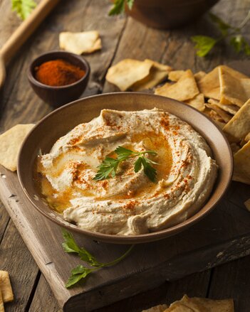 Auf dem Foto ist eine Schüssel mit Hummus zu sehen. Daneben sieht man Chips. | © SONNENTOR