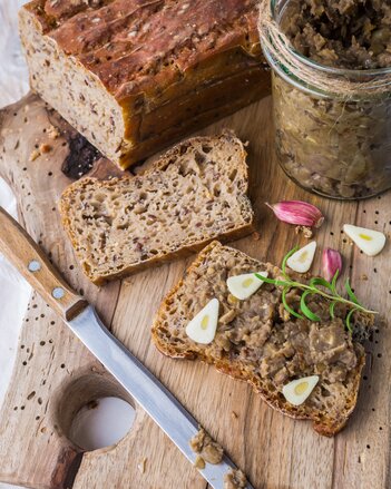 Auf dem Foto ist Brot zu sehen und daneben ein Glas Fenchel Alblinsen Aufstrich. Auf eine Brotscheibe ist der Aufstrich bereits gestrichen. | © SONNENTOR