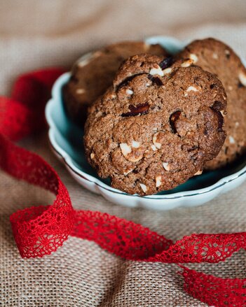 Auf dem Foto ist eine Schale mit Mandel Cookies zu sehen. Davor liegt ein satt rotes Band. | © SONNENTOR