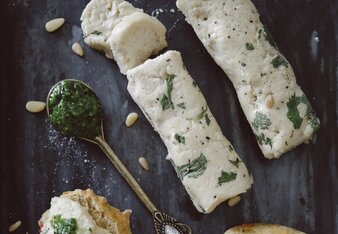 Auf dem Foto sieht man mehrere Tomatenbrötchen. Dahinter liegen zwei Rollen mit veganem Frischkäse. Auch ein Löffel mit Pesto ist zu sehen. | © SONNENTOR