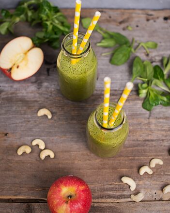 Auf dem Foto sind zwei Flaschen mit Grüner Detox Smoothie zu sehen. Daneben sind Äpfel und Cashewnüsse zu sehen. | © SONNENTOR