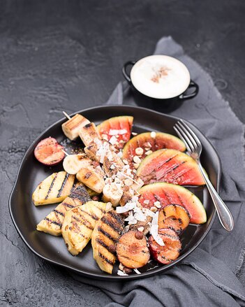 Auf dem Foto sieht man einen schwarzen Teller mit Grillobst. Daneben steht ein Schälchen mit Topfencreme. | © SONNENTOR