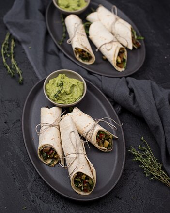 Auf dem Foto sieht man zwei Teller mit jeweils drei Stück Veggie Wraps darauf. Auf jedem Teller steht ein Schüsselschen Avocado Dip. | © SONNENTOR