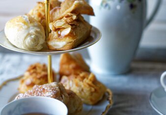 Auf dem Foto ist eine Etagere mit Apfelstrudel Fingerfood zu sehen. Davor steht eine Tasse Tee und im Hintergrund ist eine Teekanne zu sehen. | © SONNENTOR