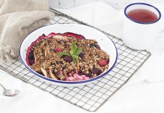 Auf dem Foto ist ein Beeren-Frühstücks-Crumble zu sehen. Daneben steht eine Tasse Tee. | © SONNENTOR