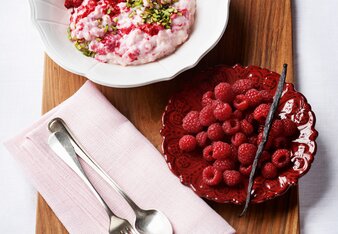 Auf dem Foto ist das rosa Beerendufteis in einer weißen Schale zu sehen. Daneben steht ein Teller mit frischen Himbeeren. | © SONNENTOR