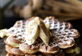 Auf dem Foto sieht man einen Teller mit mehreren Topfen-Mohn Waffeln übereinander zu sehen. Sie sind mit Bananenscheiben und Flower Power Gewürz garniert. | © SONNENTOR