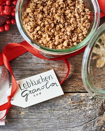 Auf dem Foto sieht man ein Glas mit Lebkuchen-Granola. Davor sieht man ein Etikett, das auf einem roten Band befestigt ist. | © SONNENTOR