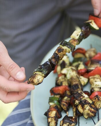 Auf dem Foto ist zu sehen, wie jemand einen Ratatouille-Spieß in der Hand hält. Auf einem Teller liegen noch weitere Spieße. | © SONNENTOR