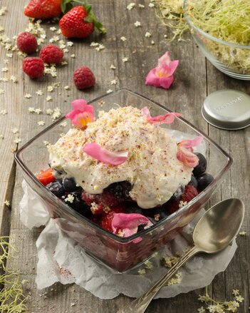 Foto von einer Schale mit Beeren-Blüten Salat. Darin sind verschiedenste Beeren mit weißer Creme und rosa Blüten zu sehen. | © SONNENTOR