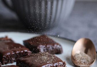 Auf dem Foto sind Brownie Chai Bites auf einem Teller zu sehen. Die Brownies werden gerade mit Chai bestäubt. | © SONNENTOR