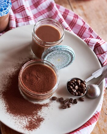 Auf dem Foto sind zwei Gläser mit Schokopudding zu sehen. Sie sind mit Kakaopulver bestreut. Daneben sind Kaffeebohnen zu sehen. | © SONNENTOR