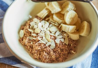 Auf dem Foto ist eine Schüssel mit Basenmüsli zu sehen. Garniert mit Bananen, und Mandelblättern. | © SONNENTOR