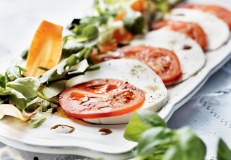 Auf dem Foto ist der Gute Laune Sommersalat mit Tomaten und Schafkäse zu sehen. Darauf sieht man das Kürbiskernöl und davor den Vogerlsalat. | © SONNENTOR