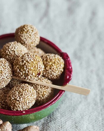 Foto von einer bunten Schüssel mit Couscous Bällchen darin. Ein Bällchen ist auf einem Holzstäbchen aufgespießt. | © SONNENTOR