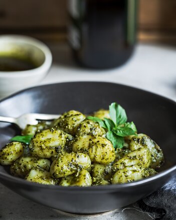 Auf dem Foto ist ein schwarzer Teller mit Gnocchi mit Kräuterpesto zu sehen. Im Hintergrund sieht man ein Schälchen mit dem Pesto. | © SONNENTOR