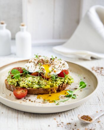 Auf dem Foto ist ein Brot zu sehen, das mit Erbsen-Mash, Tomaten und Spiegelei belegt ist. Als Topping sind diverse Kräuter zu sehen. | © SONNENTOR