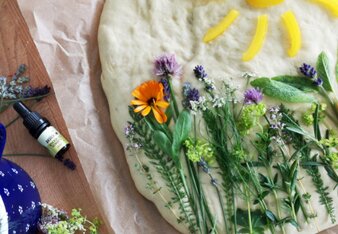 Auf dem Foto ist eine Focaccia zu sehen, auf der verschiedene Kräuter zu sehen sind. Im oberen Teil ist eine Sonne dargestellt. | © SONNENTOR