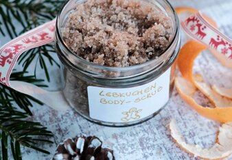 Auf dem Foto ist ein Glas Lebkuchen Body Scrup zu sehen. Daneben liegen Mandarinenschalen, Zapfen und ein Zweig. | © SONNENTOR