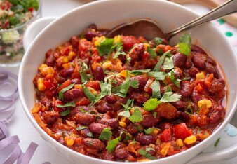 Das Chili Sin Carne besteht aus Bohnen, Mais und Sauce und ist mit grünen Blättern dekoriert in einer weißen Schüssel mit einem Löffel darin.  | © SONNENTOR