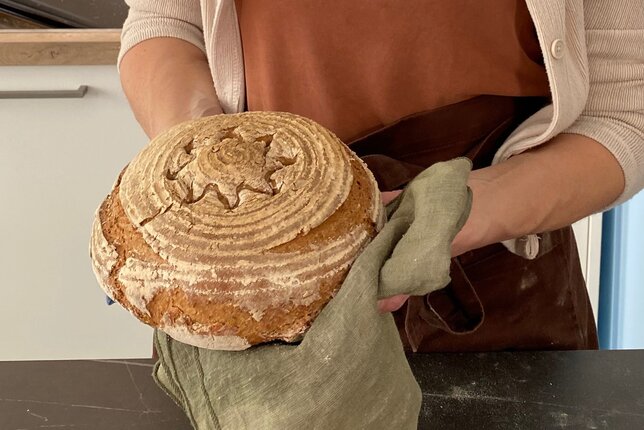 Auf dem Foto sieht man wie eine Frau einen Laib Brot mit einem Geschirrtuch hält.  | © SONNENTOR