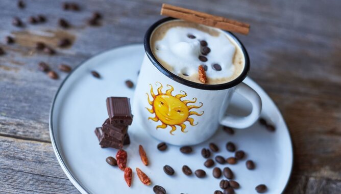 Auf dem Foto sieht man eine SONNENTOR Tasse mit Mexican Coffee darin. Daneben sind Schokostückchen, Chili und Kaffeebohnen zu sehen. | © SONNENTOR