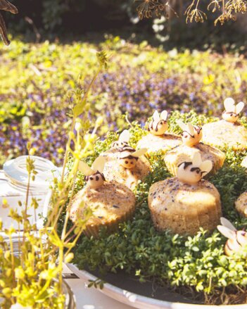 Auf dem Foto sind Muffins im Kräuterbeet zu sehen. Diese sind mit Marzipan-Bienen dekoriert. | © SONNENTOR