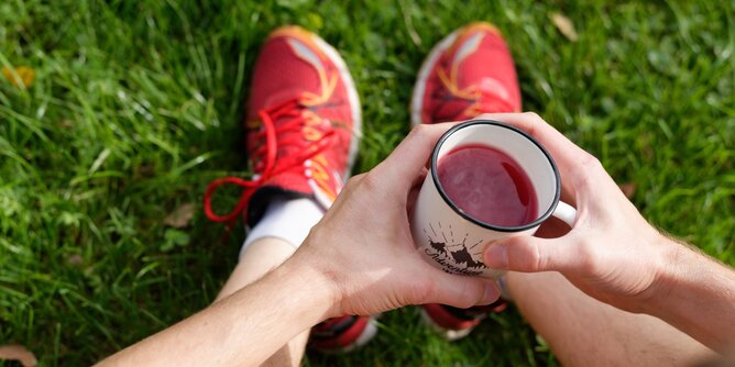 Auf dem Foto sieht man einen Mann mit Sportschuhen. Er sitzt und trinkt eine Tasse Tee. | © SONNENTOR