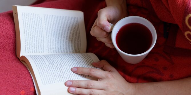 Auf dem Foto ist jemand mit einer Tasse Tee in der Hand zu sehen. Die Person liest ein Buch. | © SONNENTOR