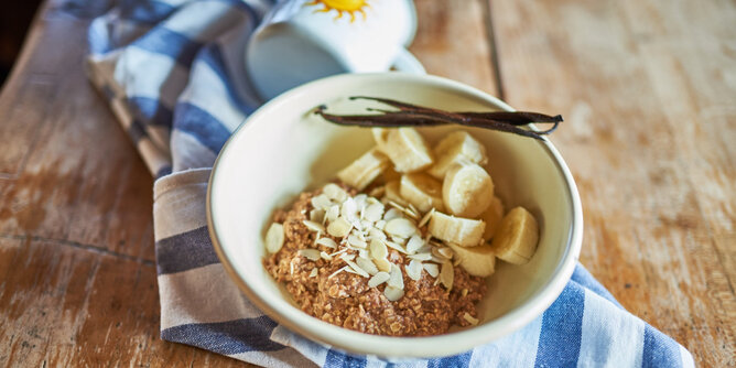 Auf dem Foto sieht man eine Schale mit Basenmüsli. Darauf sind Bananenstücke und Mandelblättchen zu sehen. Auf der Schale liegen Vanilleschoten. | © SONNENTOR